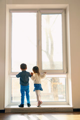 Cute little children near big window at home