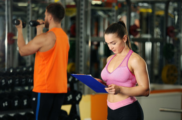 Fototapeta premium Personal trainer holding clipboard with training plan in gym