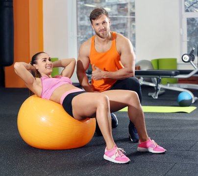 Young woman doing exercise with trainer in gym