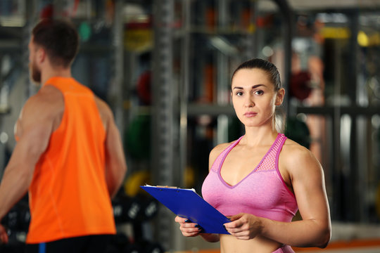 Personal trainer holding clipboard with training plan in gym