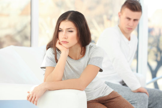 Young woman sitting on sofa after quarrel with boyfriend