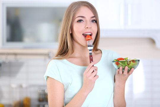 Young beautiful woman eating salad in kitchen