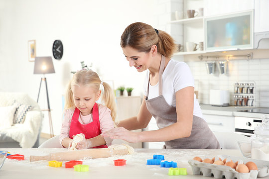 Young mother with daughter making biscuits on table