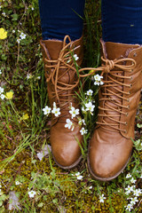 Pies de mujer con botas de piel sobre un prado florido en primavera 