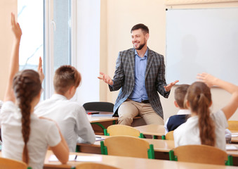 Pupils listening teacher and raising hands to answer in classroom