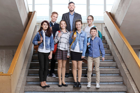 Happy pupils and teacher standing on school stairs