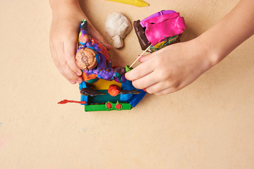 Kid is sculpting with colorful modelling clay. View from the top.