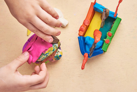 Kid is sculpting with colorful modelling clay. Close up. View from the top.