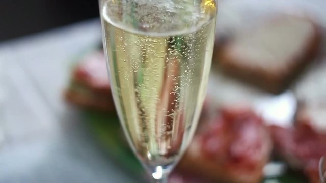 Champagne glass with sprinkling bubbles on served food background.