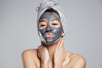 mixed race woman with clay coal grey facial cleansing mask treatment. 
