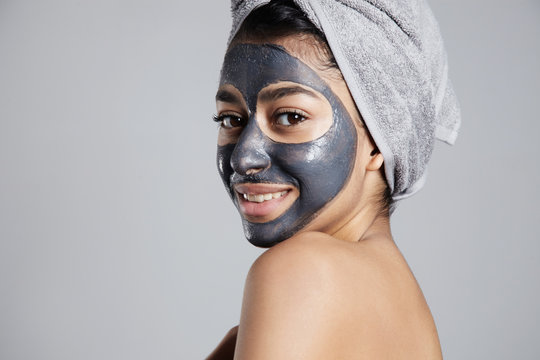 mixed race woman with clay coal grey facial cleansing mask treatment. 