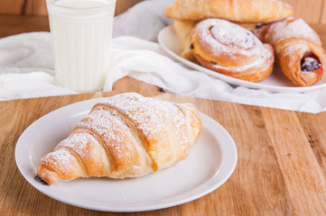 Fresh croissant with assortment of fresh pastries and glass of milk on the background. Selective focus, breakfast concept