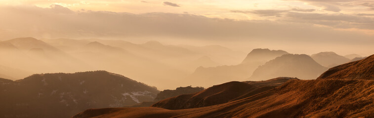 Panoramic view of mountain valley full of mist and clouds. Autumn sun glows them and makes an amazing layer perspective Tops of mountain ridge drop shadows to the slopes in autumn color. Gumbashi pass