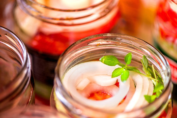 Canning fresh tomatoes with onions for winter in jelly marinade. A shot of basil leaves on top of a red ripe tomato slices and onion rings being put in jar.