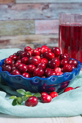 Red cranberry juice in a glass, cranberries in the blue clay bowl on the table