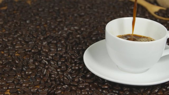panning shot of Pouring coffee from coffee pot in white cup surrounded by coffee beans