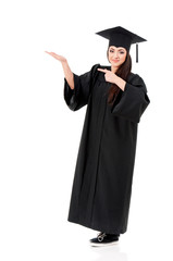 Beautiful graduate girl student in mantle showing something, isolated on white background