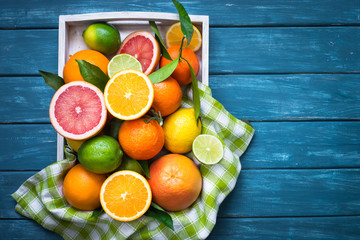 Citrus fruit in wooden tray on blue table.