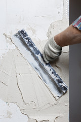 Construction worker with long trowel plastering a wall