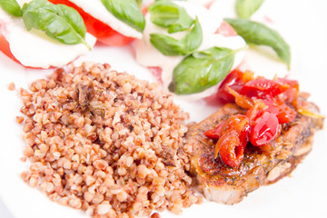 A Meal: Roast pork, kasha, and caprese salad with basil on a white plate