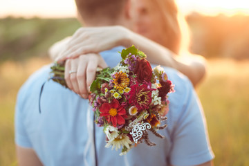 Couple hugs on sunset holding flowers