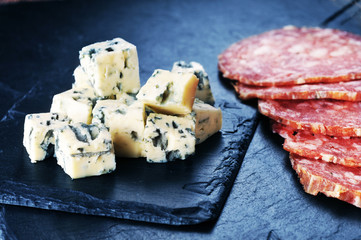 Fresh cheese and sausages on the bdark blue background