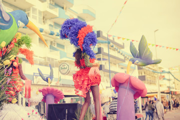 Blurry defocused silhouette of unrecognizable joyful dancing woman wearing carnival feathers costume on sunny street outdoors background. Back view