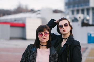 Outdoor portrait of two young beautiful girls in sunglasses and dark clothing on the background of the urban landscape.