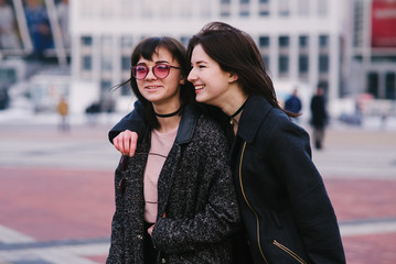 Two stylish and beautiful young girls friends wearing casual stroll around the city and smile