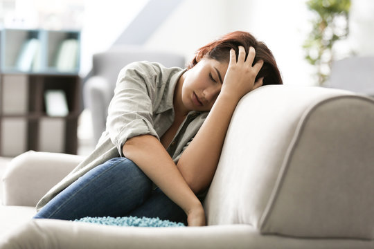 Depressed young woman sitting on sofa at home