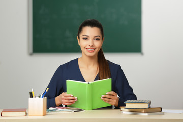 Beautiful young teacher sitting at table in classroom