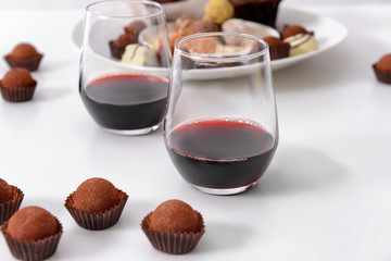 Delicious chocolate truffles and red wine on white background