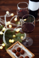 Glasses of wine and chocolates on wooden table with garland, closeup