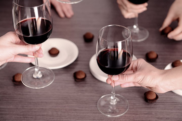 Female hands holding glasses of red wine over wooden table
