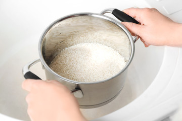 Woman holding saucepan with rice in sink