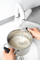 Woman rinsing rice in saucepan under running water