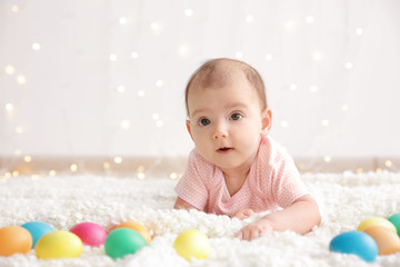 Fototapeta na wymiar Cute little baby with colorful Easter eggs lying on plaid at home