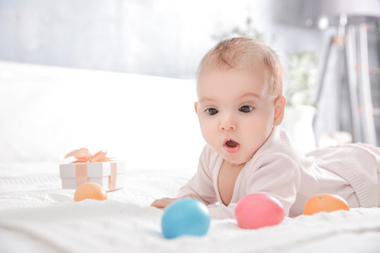 Cute little baby with Easter eggs lying on bed at home