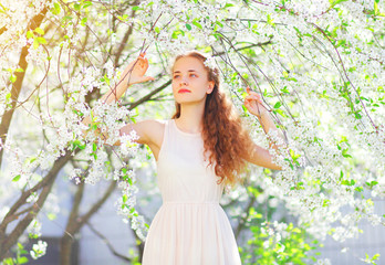 Obraz na płótnie Canvas Beautiful young woman enjoying spring flowers over garden background