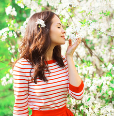Beautiful young woman enjoying smell spring flowers at garden