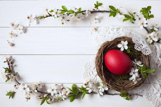 Easter white wooden background with a nest, red egg and branch with flowers, space for greeting text