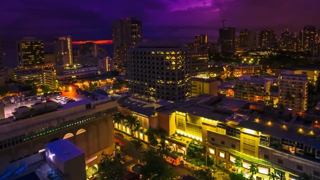 Moving time lapse of changing pink light at twilight of Waikiki cityscape in Oahu, Hawaii, United States. Sun setting to dark sky with moving clouds and stars. City night lights and nightlife concept.