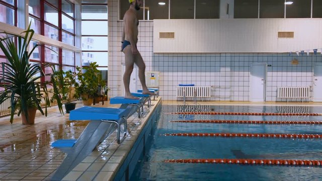 Muscular swimmer warming up and jumping into the pool and swim a distance. 4K.