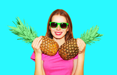 Fashion portrait pretty smiling woman and two pineapple in sunglasses over blue background