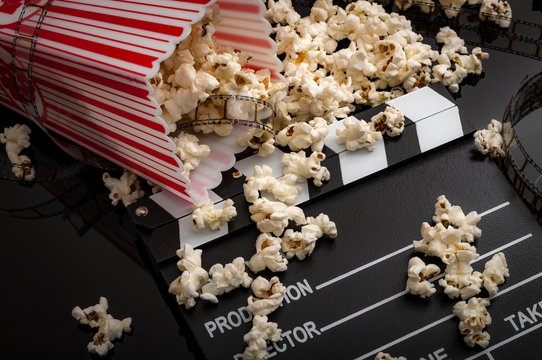 Movies and entertainment concept with dropped box of popcorn on film strip and clapper board and pop corn scattered everywhere