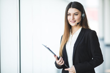 Photo of beautiful young call center operator standing. Woman with headphones looking at camera and...