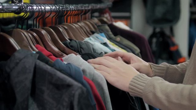 Men sweaters and shirts in different colors on hangers in a retail clothes store, man choose hoodies close up in shop
