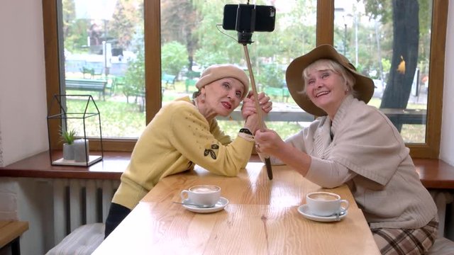 Women taking selfie in cafe. Senior ladies shaking hands. Years pass but friendship remains.