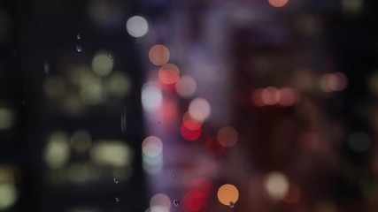 Rain drips down the window of a high rise building in a city. Shallow depth of field with bokeh