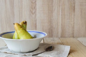 side view of two green ripe pears in bowl dish and spoon on linen doily on wooden table with copy...